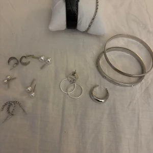 Smyckeset med armband och örhängen i silver - Ett elegant smyckeset bestående av tre silverfärgade armband, örhängen och en klocka.  Setet inkluderar både klassiska ringar och pärlörhängen samt ett stilrent armband med stenar. Perfekt för att komplettera din look med en touch av elegans. 