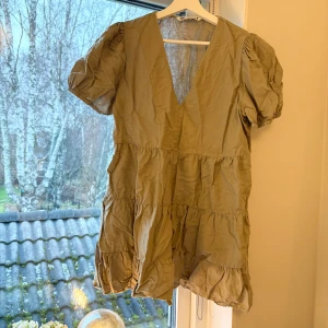 Beige klänning från Zara - Säljer en superfin beige klänning från Zara i storlek M. Den har en v-ringad design med korta puffärmar🌼