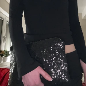 Svart glittrig kuvertväska - Snygg svart kuvertväska med glittriga paljetter, perfekt för festliga tillfällen. Väskan har en  dragkedja i guld som ger en lyxig touch. Perfekt nu till nyår!!
