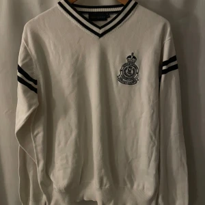 Vit tröja från Henri Lloyd - Säljer en stilren vit tröja från Henri Lloyd med mörkblåa ränder på ärmarna och en snygg broderad logga på bröstet. Tröjan har en v-ringad krage med ribbade detaljer och är i storlek L. Perfekt för en casual look eller en dag på stan.💙