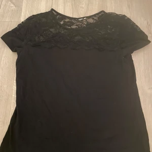 Svart topp med spetsdetaljer - Snygg svart topp med spetsdetaljer över axlarna och bröstet. Kortärmad design som passar perfekt för både vardag och festliga tillfällen. En stilren och elegant look.