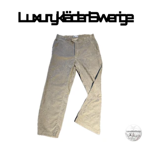 Beige byxor från ACG Nike 34 strlk - Säljer ett par beige byxor från ACG med en avslappnad passform. Byxorna har en praktisk ficka bak med knapp och är tillverkade i en blandning av bomull och polyester. Perfekta för en casual look.