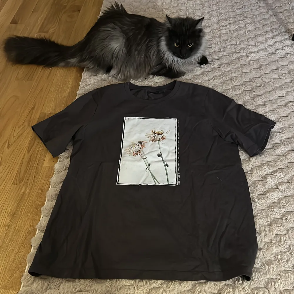 Snygg svart t-shirt med ett stilrent blommotiv på framsidan. . T-shirts.