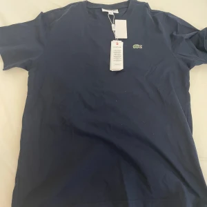 Lacoste T-Shirt - Lacoste t-shirt mörkblå storlek L men passar bättre på M. Alla etiketter finns för mer bilder skriv är det bara att fråga. Helt oanvänd