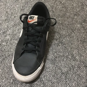 Svarta Nike sneakers - Säljer ett par svarta Nike sneakers i bra skick. De har en klassisk design med vit sula och vit swoosh på sidan. Skorna har svarta snören och en bekväm passform, perfekta för vardagsbruk eller träning. Lite slitage på sulan men annars i fint skick.