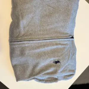 Säljer en snygg grå hoodie från Polo Ralph Lauren i  nyskick. Den har en dragkedja framtill och det klassiska broderade logotypen på bröstet. Perfekt för en avslappnad stil och passar till alla säsonger. Storleken är custom fit, vilket ger en bekväm passform. Storlek L passar även M, pris går att diskutera! Möts upp i Stockholm eller fraktas