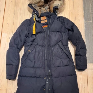 Mörkblå dunjacka från Parajumpers - Säljer en dunjacka från Parajumpers med pälsfodrad huva och gul detalj vid halsen. Jackan har dragkedja och knappar framtill samt flera praktiska fickor. Mycket fint skick. Varm och skön.