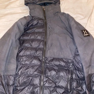 Svart pufferjacka från Haglöfs - Säljer en svart pufferjacka från Haglöfs med dragkedja och hög krage. Jackan har en quiltad design och är perfekt för kyligare väder. Den har en praktisk huva och är långärmad. Dold bröstficka;)