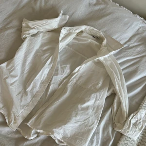 Vit skjorta - Klassisk vit skjorta med långärmad design. Perfekt för en stilren look, oavsett tillfälle. Skjortan har en enkel och tidlös stil med knappar framtill. Från asos