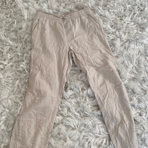 Beige byxor med resårmidja - Säljer ett par bekväma beige byxor i bra skick. De har en elastisk midja för extra komfort och är perfekta för en avslappnad stil. Materialet ser ut att vara lätt och luftigt, vilket gör dem idealiska för vår och sommar. Passformen är loose, vilket ger en skön och ledig känsla.
