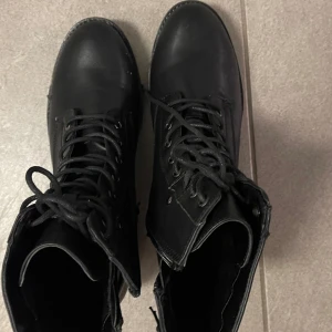 Svarta boots med snörning - Säljer ett par snygga svarta boots i skinn med snörning framtill. De har en robust sula som ger bra grepp och är perfekta för höst och vinter. Skorna är i mycket bra skick och passar både till vardags och lite tuffare outfits. Perfekt för dig som vill ha en stilren look med en edge!