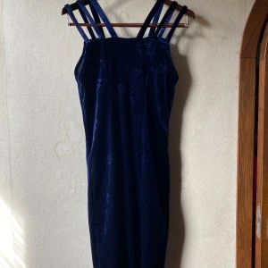 Mörkblå vintage klänning i sammet - Elegant mörkblå klänning i sammet med subtilt blommönster. Köpt second hand, men inte använd av mig. (Bilderna är på förra säljaren) Storleken är uppskattad, se mått. Längd: 99cm, byst: 92cm, midja: 88cm, höft: 104cm
