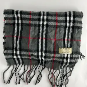 Säljer en klassisk grå rutig halsduk från Burberry i 100% lammull. Den har ett tidlöst mönster med inslag av svart, vitt och rött. Perfekt för att hålla sig varm under kyliga dagar. Fransen ger en extra touch av stil. Passar både höst och vinter. 🧣✨