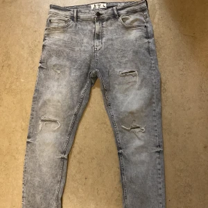Grå slitna jeans - Säljer ett par grå jeans i bra  skick med coola slitningar på framsidan. Jeansen är i slimfit, det är bara att skriva vid funderingar