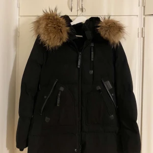 Svart vinterjacka med pälsdetaljer - Säljer en snygg svart vinterjacka med pälsdetaljer på huvan. Jackan har dragkedja och knappar framtill, samt flera praktiska fickor. Perfekt för kalla vinterdagar! 🖤jackan är helt ny, oanvänd från hollies orginal prisr: 3 750 kr.  