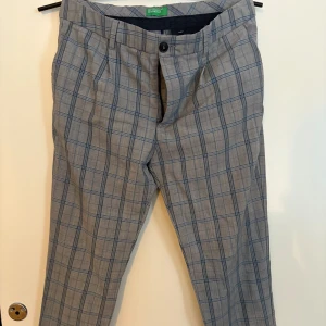 Grå rutig byxa  - Snygga grå byxor med rutigt mönster. De har en klassisk passform med knappar och dragkedja framtill. Perfekta för en stilren look. Storlek 48