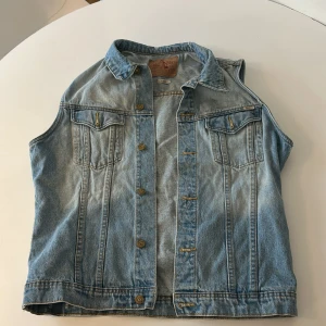 Jeansväst med knappar - Snygg jeansväst med klassisk krage och knappar framtill. Västen har två bröstfickor med lock och knappdetaljer. Perfekt för en avslappnad stil.