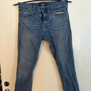 Blå jeans från Hollister - Snygga blå jeans från Hollister med klassisk femficksdesign och knappgylf. Perfekta för en avslappnad stil. De har en straight passform och är tillverkade i slitstarkt denim. Storlek 30/30