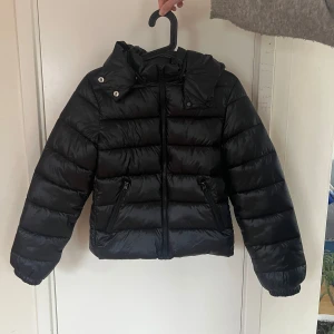 Svart pufferjacka från Gina Tricot - Säljer en svart pufferjacka från Gina Tricot. Jackan har en dragkedja framtill och två fickor med dragkedjor, luvan går att ta av. Helt oanvänd och passar bra på mig som är xs/s! Nypris:499