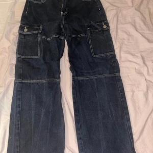 Svarta cargopants från Shein - Snygga svarta cargopants från Shein med vita sömmar och flera praktiska fickor. Byxorna har en loose passform och är perfekta för en avslappnad stil. Tillverkade i ett slitstarkt material som ger en cool look.