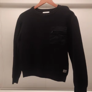 Svart tröja från Zara med bröstficka - Säljer en svart tröja från Zara i storlek 11-12 år. Tröjan har en praktisk bröstficka med dragkedja och är ribbad för extra stil. Perfekt för en cool och avslappnad look.