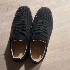 Svarta sneakers med nitar - Snygga svarta sneakers från Christian Louboutin med nitar på ovansidan och den ikoniska röda sulan. Skorna har snörning och är tillverkade i mocka. Dem är mer använda än på bilden. Pris kan diskuteras vid snabb affär 