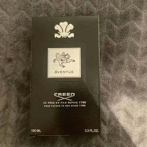 Creed Aventus Parfym 100 ml - Exklusiv Creed Aventus parfym i en elegant flaska på 100 ml. Flaskan har en stilren design med svart och silverdetaljer samt en distinkt logotyp. Perfekt för den som söker en lyxig och tidlös doftupplevelse. Skriv innan köp
