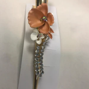 Strass Hårspännen med blommor  - Säljer tre eleganta hårspännen med blommotiv i olika färger: orange, rosa och grå. Varje spänne har en blomma dekorerad med strass och en guldig bas. Perfekt för att ge en extra touch till din frisyr.  65kr/st . Helt ny 