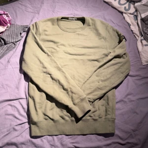 Olivgrön tröja från Stone Island Junior - Säljer en olivgrön tröja från Stone Island Junior. Tröjan har en rund halsringning och långa ärmar. Den är dekorerad med det ikoniska Stone Island-märket på ärmen. Perfekt för en stilren och avslappnad look. Säljer för att den inte passar längre. Skick 9,5/10