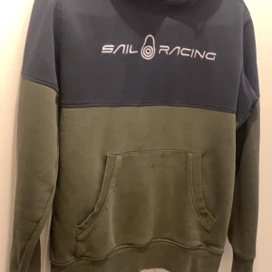 Grön och blå hoodie från Sail Racing - Säljer en grön och blå hoodie från Sail Racing i storlek M. Tröjan har en stor ficka framtill och en bekväm huva. Perfekt för kyliga dagar. Hör av dig vid intresse! Ingen skador absolut 