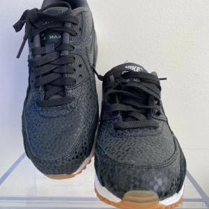 NIKE WMNS AIR MAX 90 PREM - Snygga svarta Nike Air Max sneakers med prickigt mönster och klassisk snörning. Skorna har en vit sula med brun undersida och tydlig Nike-logga på hälen. Perfekta för en stilren look.