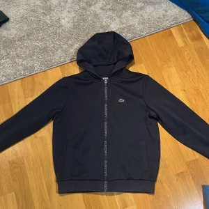 Huvtröja från Lacoste Sport - Tja, säljer en stilren svart huvtröja från Lacoste Sport med dragkedja och luva. Tröjan har en unik detalj där det på dragkedjan står Lacoste. Tröjan är i nyskick och finns inga tecken på användning trots att den använts 2 gånger. Säljer då den är för liten!! Priset kan alltid diskuteras💫🤝