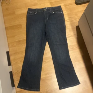 Mörkblå bootcut jeans från Style & Co - Snygga mörkblå jeans från Style & Co med dekorativa bakfickor och knappdetaljer. Tillverkade i en bomullsblandning med polyester och spandex för extra komfort och stretch. Perfekta för en avslappnad stil.