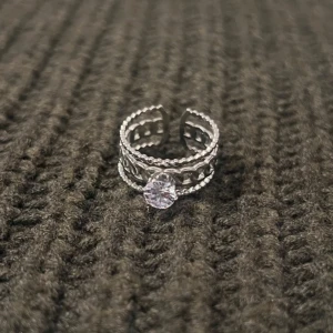 Braided Elegance - Silver Ring with Stone - US storlek 7, diameter 17,3 mm, omkrets 54,4 mm. Denna sofistikerade ring har ett vackert flätat motiv som ramar in en gnistrande sten i mitten. Den justerbara designen gör den både bekväm och tidlös.