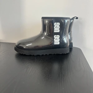 Svarta boots från UGG - Snygga svarta boots från UGG med en glansig yta och tydlig logotyp på sidan. De har en robust sula och är fodrade för extra värme. Perfekta för kyligare dagar. Enbart använda 2 gånger, nypris kostar dem 2500kr
