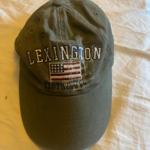 Grön keps från Lexington - Snygg grön keps från Lexington med broderad text och amerikansk flagga på framsidan. Perfekt för en avslappnad stil. Justerbar passform för optimal komfort.