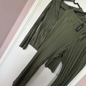 Boohoo set  - Säljer jättefin plisserad skjorta med utsvängda armar plus byxorna till den i färgen Khaki/Olivgrön. Det är ett set, prislappen finns kvar och helt oanvända. Storlek på skjortan är 42 Storlek på byxan är 44