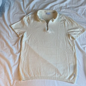 Beige pikétröja från Jack & Jones - Säljer en stilren beige pikétröja från Jack & Jones. Tröjan har korta ärmar och en dragkedja vid halsen för en modern look. Perfekt för en avslappnad stil.