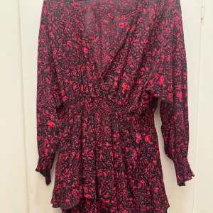 Svart och röd klänning från Zara - Snygg svart och röd klänning från Zara med ett abstrakt mönster. Klänningen har långa ärmar och en v-ringad design som ger en elegant touch. Perfekt för att sticka ut med sin unika stil.