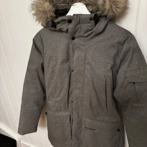 Grå parkajacka från Everest - Säljer en grå parkajacka från Everest med avtagbar huva och fuskpäls. Jackan har långa ärmar och flera praktiska fickor med dragkedja. Perfekt för kalla dagar med sin varma och skyddande design. Hör av dig vid intresse! ❄️