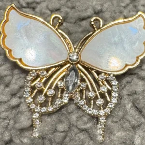 Fjärilsformad brosch i guld och pärlemor - Elegant fjärilsbrosch med vingar i pärlemor och detaljer i guld. Smyckad med glittrande stenar som ger en lyxig känsla. Perfekt accessoar för att lyfta vilken outfit som helst.