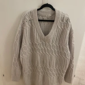 Filippa K ljusgrå tröja - Stickad tröja med v-ringning och ett vackert kabelmönster. Tröjan har en avslappnad passform och en längre längd. Perfekt för höst- och vinterdagar. Dem är i riktigt fint skick. Storlek XS. Rökfritt hem. Skickar paket som spårbart.
