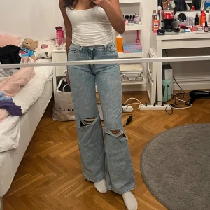 Blå jeans med vida ben - Snygga blå jeans med vida ben och slitna detaljer på knäna. De har en hög midja och klassisk femficksdesign. Perfekta för en avslappnad stil.