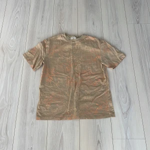 Beige t-shirt med mönster från H&M - Säljer en beige t-shirt från H&M med ett subtilt mönster i orange. T-shirten är kortärmad och har en avslappnad passform. Perfekt för en casual look.