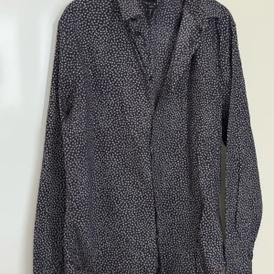 H&M - Snygg mönstrad skjorta från H&M i mörkblått med små vita och röda detaljer. Skjortan har en slim fit passform och långa ärmar, perfekt för en stilren look. Knappar framtill för enkel stängning.