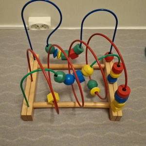 Färgglad kulbana i trä - Säljer en färgglad kulbana i trä med flera slingrande metalltrådar i olika färger. Kulorna är i olika former och färger som röd, blå, grön och gul. Perfekt för att stimulera barnens motorik och koordination.