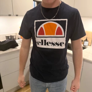 Marinblå t-shirt från Ellesse - Marinblå t-shirt från Ellesse med deras ikoniska logga i orange och rött på bröstet. 