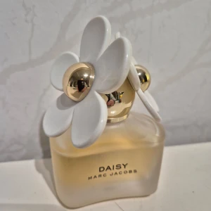 Daisy parfym från Marc Jacobs - Säljer en Daisy parfym från Marc Jacobs. Flaskan är elegant med en frostad glasdesign och har en unik kork dekorerad med vita blommor och guldfärgade detaljer. Perfekt för den som älskar en fräsch och blommig doft. Testad ca 10 sprut. Nypris 1150kr
