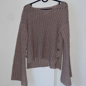 Beige stickad tröja med knappar - Säljer en mysig beige stickad tröja med dekorativa knappar på sidan. Tröjan har en luftig stickning och långa utsvängda armar som är en så fin detalj!😊 Tröjan är väldigt ljuslila! Märket på tröjan kan jag inte tyda men sista bilden visar hur märket ser ut!