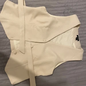 Beige väst från Boohoo - Snygg beige väst från Boohoo med knytband i midjan. Perfekt för att ge en stilren touch till din outfit. Västen har en elegant design och är tillverkad i ett mjukt material.